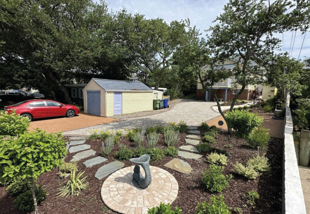 Landscaped front yard with curved stone walkway, garden beds, and a central mermaid statue in a residential property