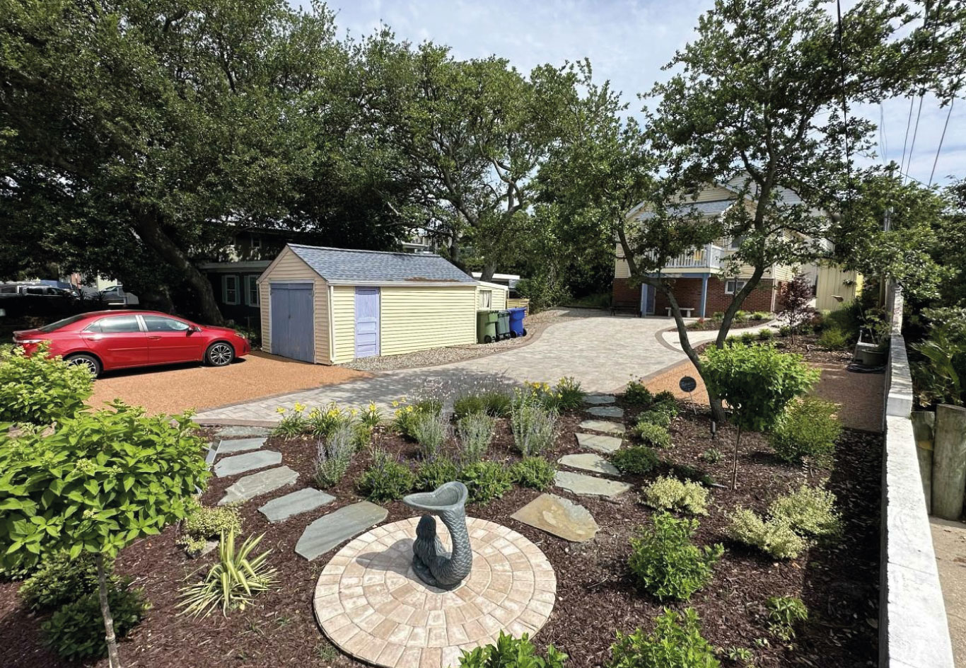 Landscaped front yard with curved stone walkway, garden beds, and a central mermaid statue in a residential property