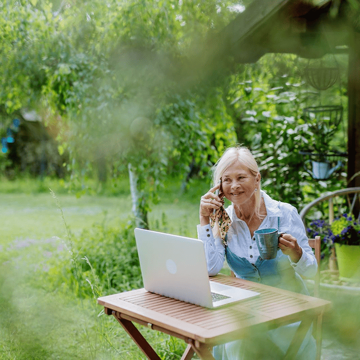 Senior woman outdoors on laptop and phone in garden