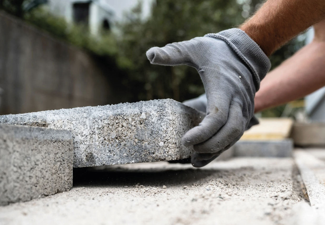 Hand placing a concrete paver during patio installation