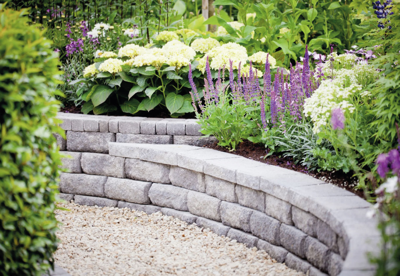 Raised garden beds bordered by stone retaining walls and filled with colorful blooms