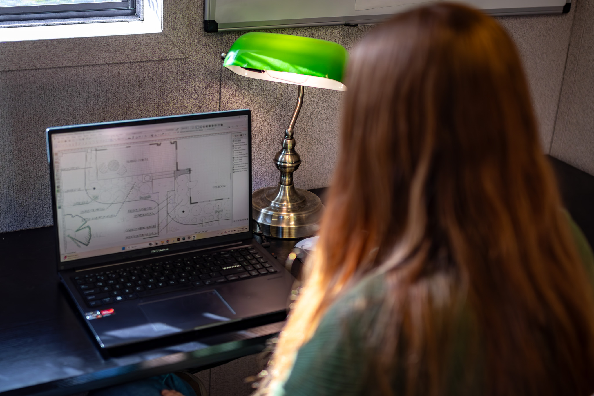 Woman sitting at laptop with landscape design plan open